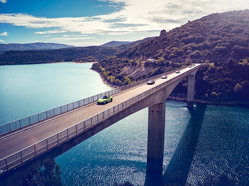 Porsche cars driving in convoy along a bridge