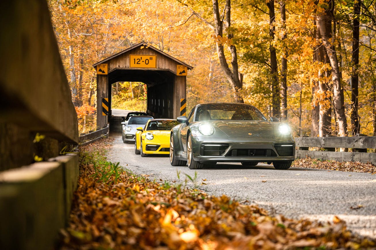 Three Porsche 911s driving passing covered bridge